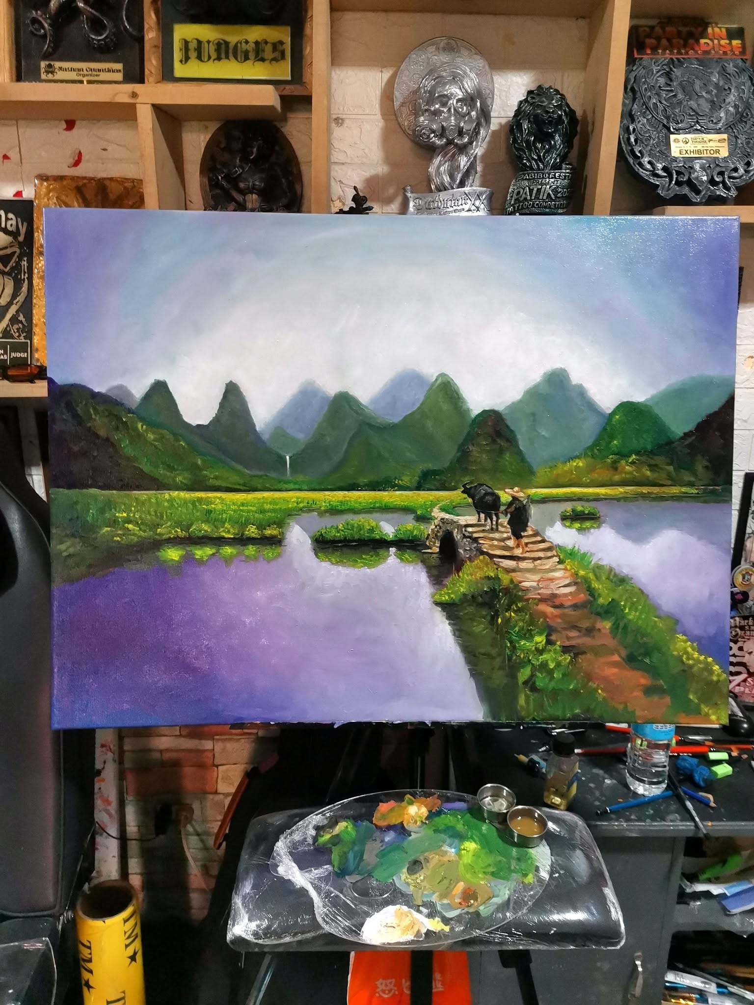 Oil painting of a farmer and carabao below green mountains